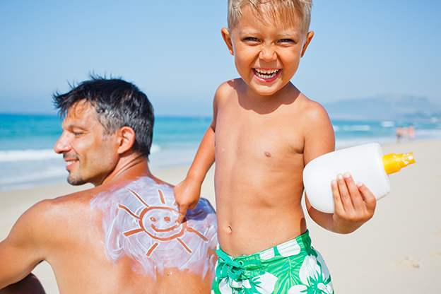 Padre e hijo en la playa con un bote de protector solar
